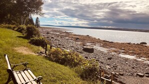 A bench on a grassy area overlooking a rocky shoreline with a body of water and distant land.