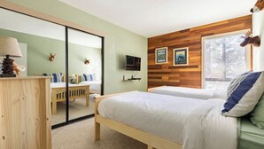 Une chambre avec deux lits, une tête de lit en bois, un miroir, une télévision et une fenêtre avec des stores.