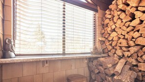Une cuisine avec une fenêtre, une pile de bois de chauffage et deux tabourets en bois.
