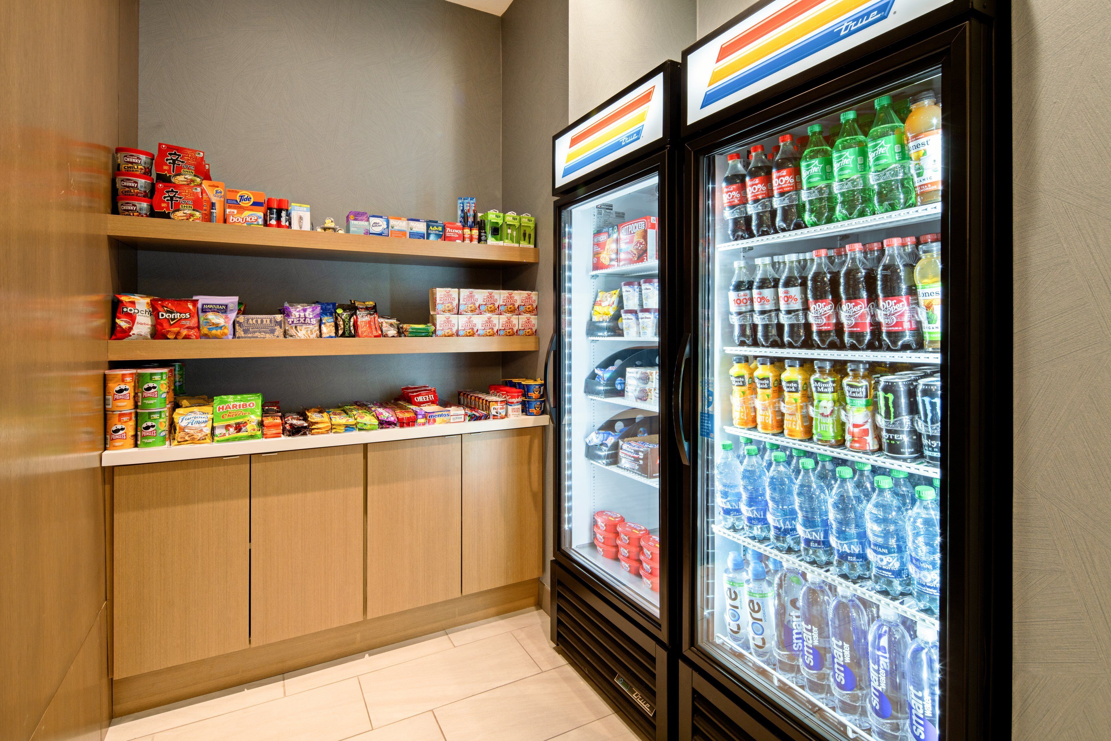A snack and beverage display area with shelves stocked with various snacks and a refrigerator filled with bottled water and sodas.