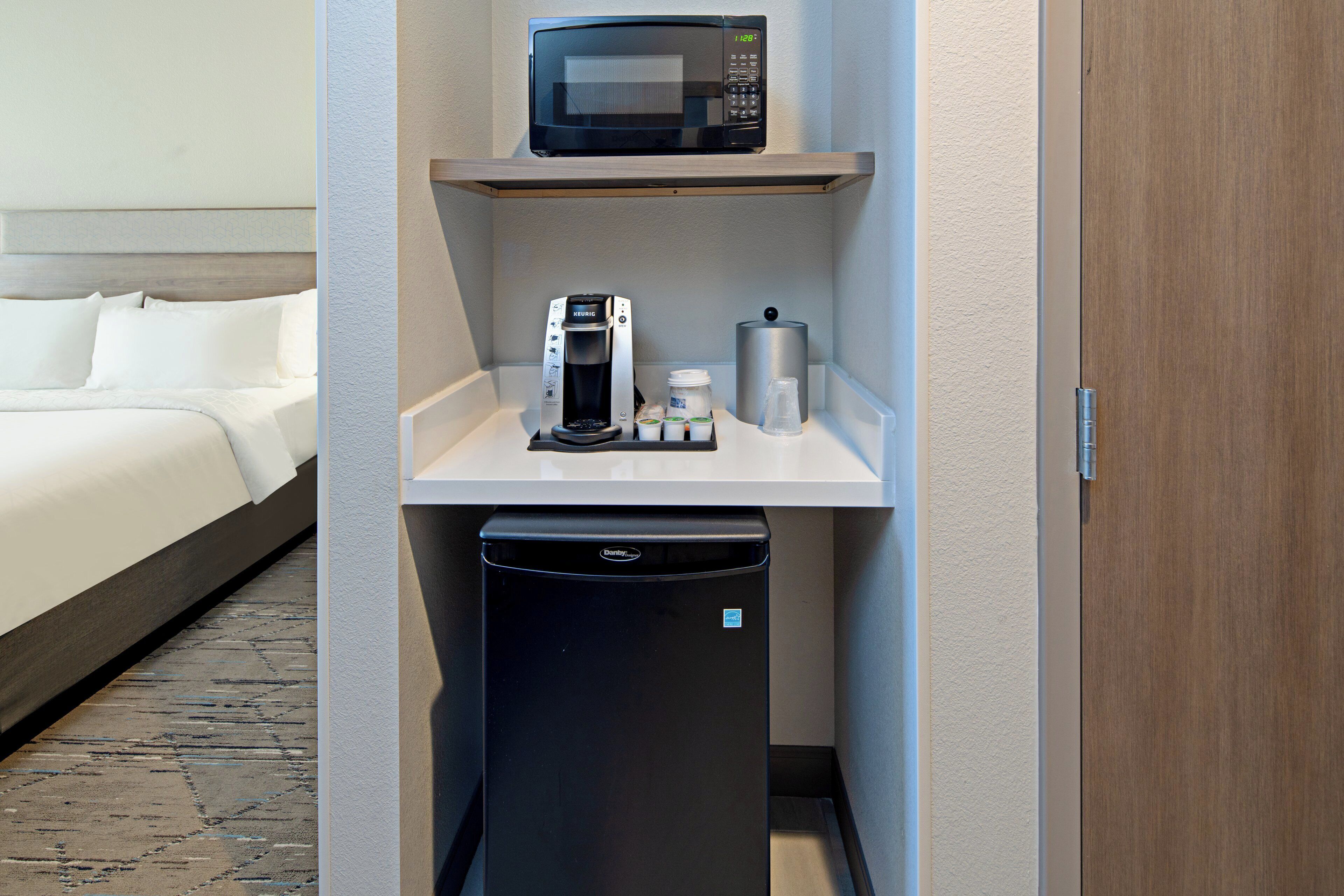 A compact kitchenette with a microwave, coffee maker, and a trash bin.
