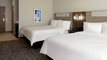 A hotel room with two beds, a wooden floor, a wall-mounted artwork, and a nightstand with a phone.