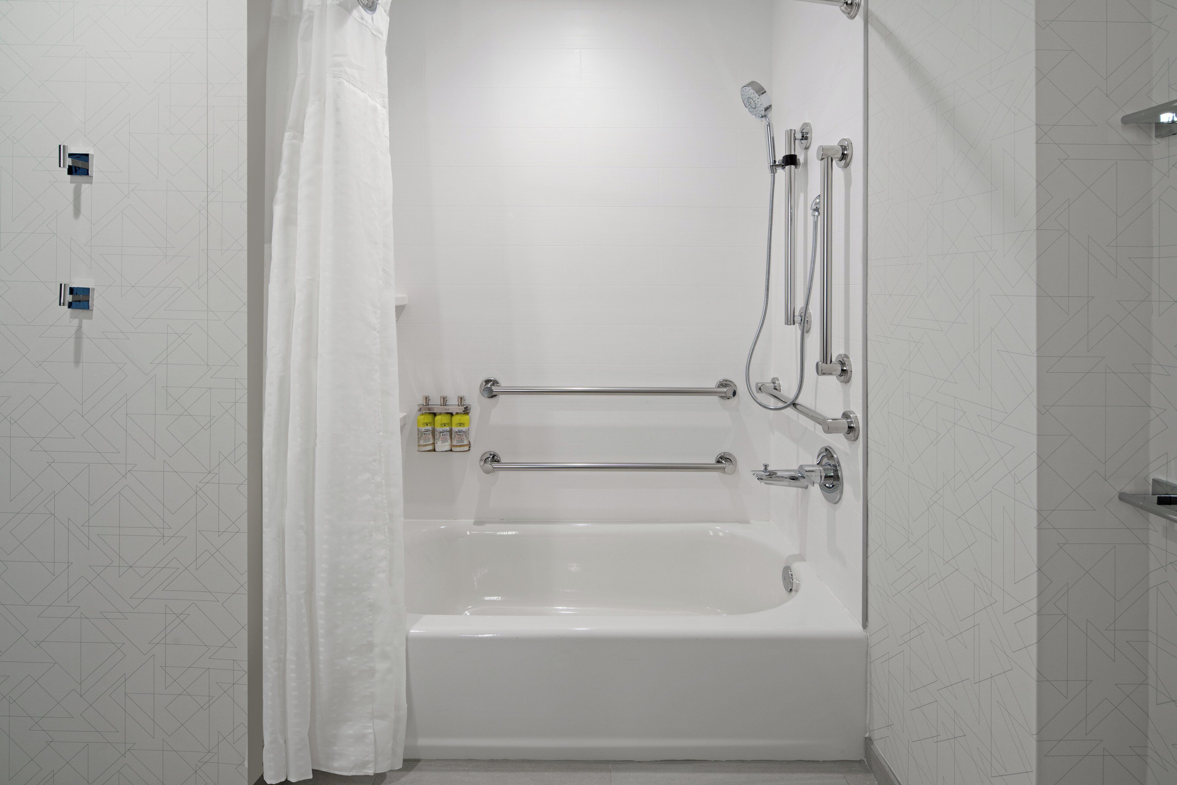 A white bathtub with a showerhead, a towel rack, and a bottle of shampoo.
