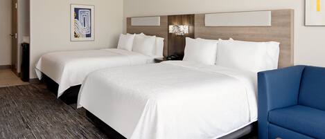 A hotel room with two beds, a blue sofa, a wooden coffee table, and a wall-mounted light fixture.