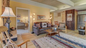 A cozy living room with a sofa, coffee table, and a rug. There is a door leading to another room and a refrigerator in the background.