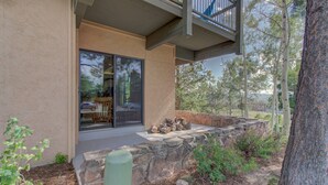 A modern building with a stone retaining wall, a glass door, and a balcony overlooking a landscaped area with trees.