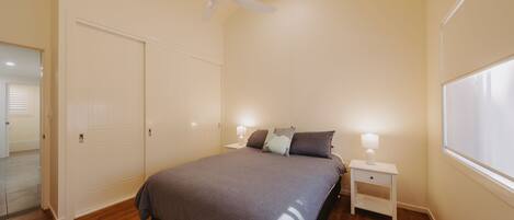 Quarto com cama, mesas de cabeceira, ventilador de teto e janela.