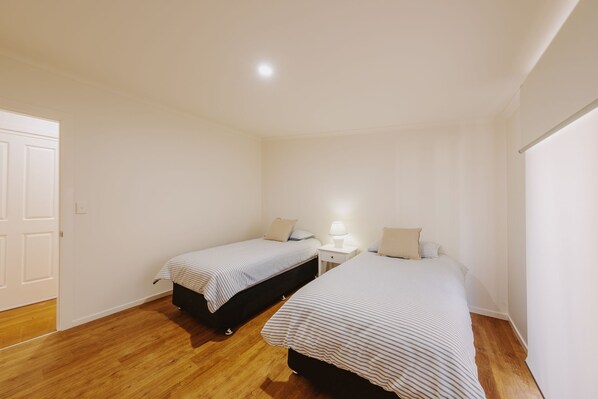 A bedroom with two single beds, a bedside table with a lamp, and a wooden floor. - Enjoy sitting on the balcony listening to the ocean waves with the sea breeze (Diamond Beach)