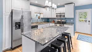 Eine moderne Küche mit weißen Schränken, Edelstahlgeräten, Granit Arbeitsplatten und einer Bar mit Barhocker.