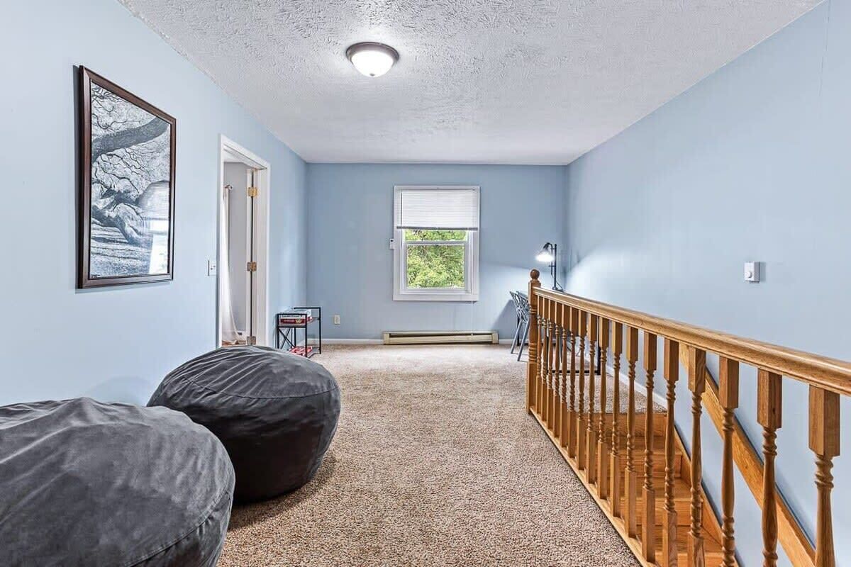 A room with a wooden staircase, a door leading to another room, a window with blinds, and a framed picture on the wall.