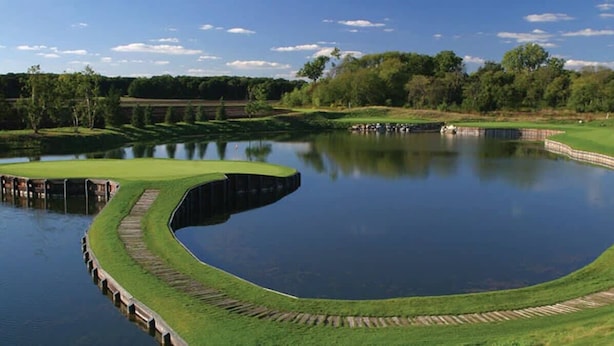 Ein Golfplatz mit Teich, umgeben von Bäumen und einem klaren Himmel.