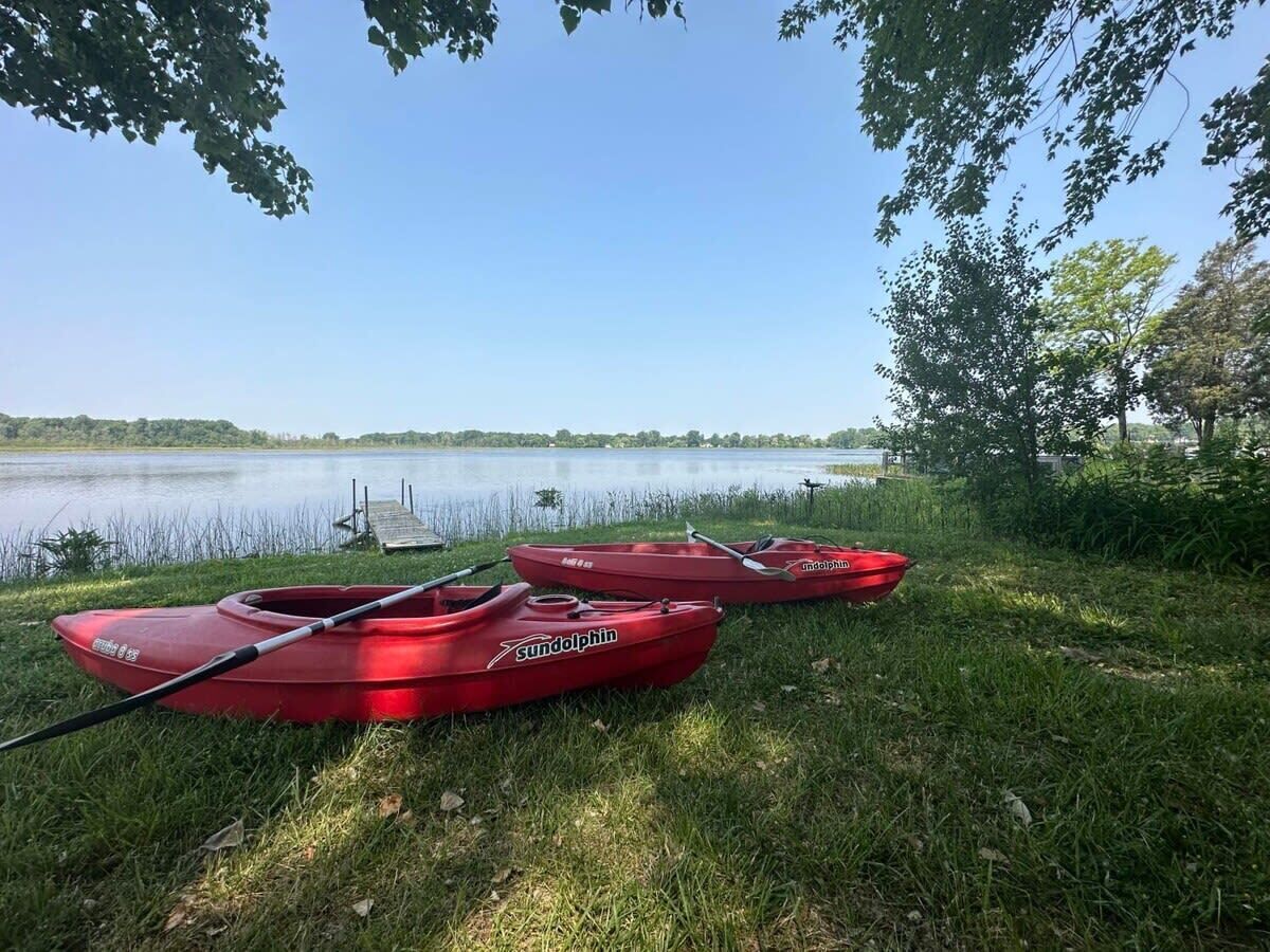 Trois kayaks rouges, accompagnés de leurs pagaies, sont appuyés contre une rive herbeuse au bord d’un lac paisible.