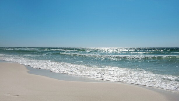 Ein Strand mit blauem Himmel und ruhiger Wellenbewegung.