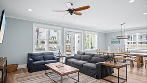 Een ruime woonkamer met een groot raam, een plafondventilator en een eetgedeelte met een tafel en banken.