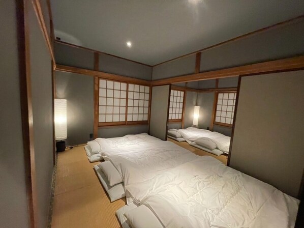 A traditional Japanese-style room with tatami flooring, shoji screens, and a futon bed arrangement.