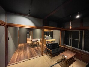 A spacious room with a wooden floor, a black leather sofa, a small table, and a large window.