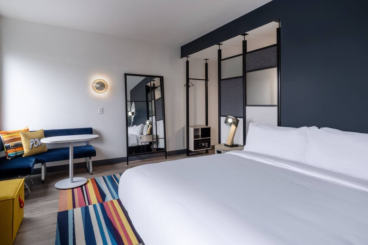 A modern hotel room with a large bed, a round table, a sofa, and a mirror.