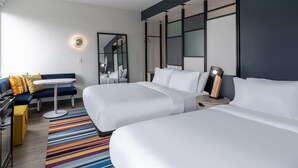 Ein Hotelzimmer mit zwei Betten, einem kleinen Tisch, einem Sofa, einem Spiegel und einem Nachttisch mit einer Lampe.