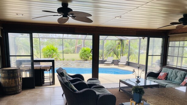 Une pièce spacieuse dotée d’une grande porte vitrée donnant sur un jardin avec une piscine, du mobilier d’extérieur et un ventilateur de plafond.