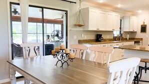 Une cuisine moderne avec des meubles blancs, une table à manger en bois et un ventilateur.