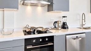 A modern kitchen with a built-in oven, a dishwasher, a kettle, and a coffee maker.