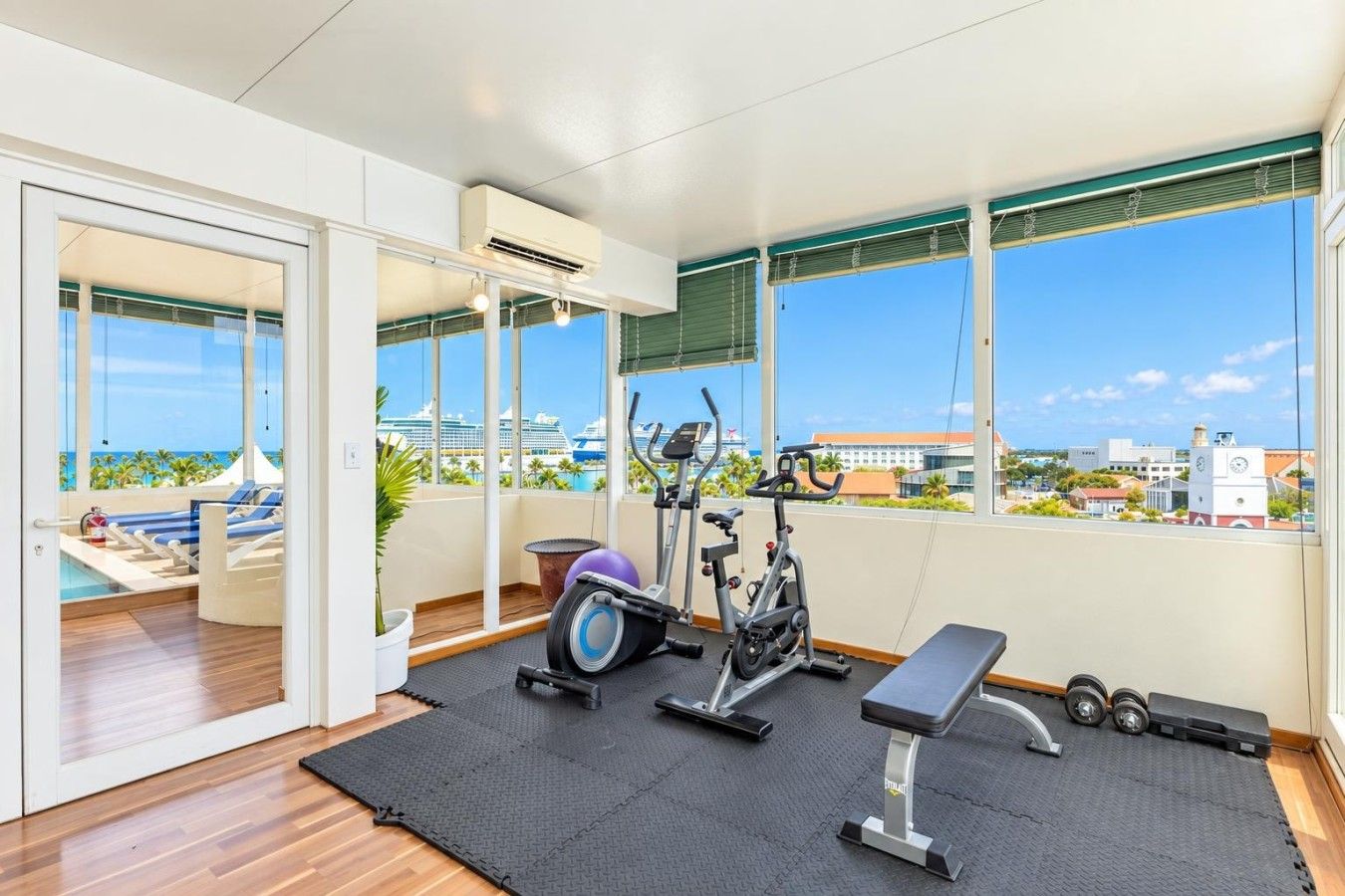 A gym with exercise equipment, a bench, and a view of the ocean and buildings.