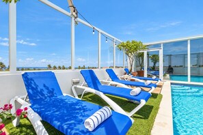 A rooftop pool area with sun loungers and a clear view of the ocean.