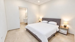 Ein Hotelzimmer mit Bett, Nachttischen und einem durch eine offene Tür einsehbaren Badezimmer.