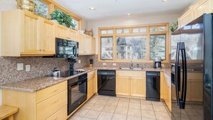 Una cocina moderna con armarios de madera, encimeras de granito, un refrigerador negro y un lavavajillas.