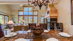 A dining area with a wooden table set for four, a fireplace, and large windows offering a view of trees. - Deluxe 3 BDR/3 BA Townhome Just Steps from Skiing in Mountain Village (Mountain Village)