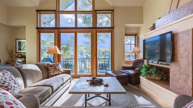 A spacious living room with a large window, a flat-screen TV mounted on the wall, and a comfortable seating area with sofas and a coffee table. - Deluxe 3 BDR/3 BA Townhome Just Steps from Skiing in Mountain Village (Mountain Village)