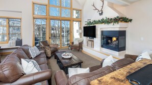 A cozy living room with a fireplace, leather sofas, and large windows offering a view of the outdoors. - 3 BDR Mountain Village Townhome, Steps from Skiing and Dining (Mountain Village)
