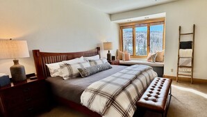 A bedroom with a large bed, a bench, a window with a view of snow-covered trees, and a wooden ladder against the wall. - 3 BDR Mountain Village Townhome, Steps from Skiing and Dining (Mountain Village)