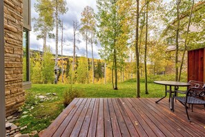 A wooden deck with a table and chairs, surrounded by trees and a stone building. - Ideal Location- 3 BDR Mountain Village Townhome Steps from Skiing (Mountain Village)