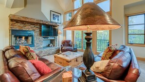 A spacious living room with leather sofas, a large table, a fireplace, and a large window with a view. - Spacious 3 BDR Mountain Village Townhome Just Steps from Skiing (Mountain Village)