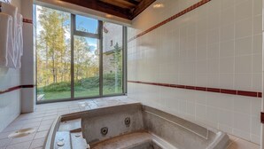 A modern bathroom with a stone bathtub, large windows, and a view of trees. - Spacious 3 BDR Mountain Village Townhome Just Steps from Skiing (Mountain Village)