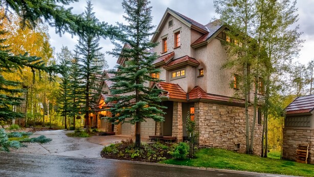 A two-story stone house with a stone foundation and a red roof, surrounded by a well-maintained lawn and tall evergreen trees. - Spacious 3 BDR Mountain Village Townhome Just Steps from Skiing (Mountain Village)