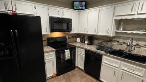 Uma cozinha moderna com armários brancos, uma geladeira preta, micro-ondas, forno e lava-louças.