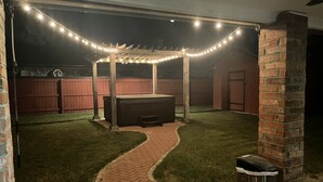 Um quintal com um caminho de tijolos, uma pérgola de madeira e luzes de corda.