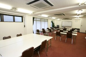 Un salón de conferencias con una larga mesa, varias sillas, una pizarra y una pantalla de proyector.