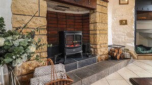 A stone fireplace with a black wood-burning stove, a wicker bench, and a basket of firewood. - Runnymede (Tewkesbury)