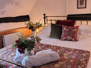 A neatly made bed with floral bedding, a vase with flowers, and a framed picture on the wall. - Runnymede (Tewkesbury)