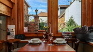 A dining table set with plates, wine glasses, and a bottle, with a view of a brick building and greenery outside. - Runnymede (Tewkesbury)