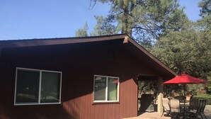 A wooden cabin with two windows, a patio with a red umbrella, and a fire pit. - Single Story Chic' One mile from Downtown,  with Tesla 220v Outlet in Garage (Prescott)