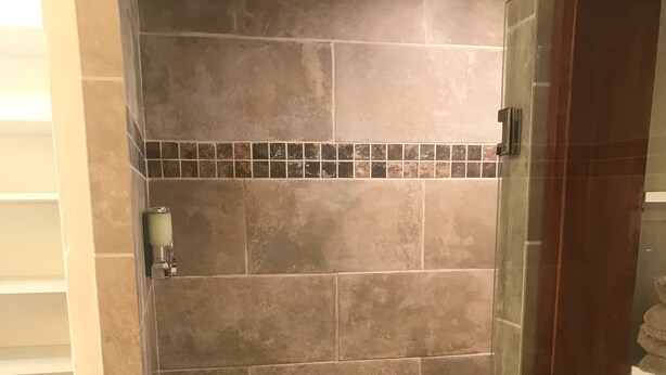 A shower area with tiled walls and floor, a glass door, and a towel rack. - Single Story Chic' One mile from Downtown,  with Tesla 220v Outlet in Garage (Prescott)