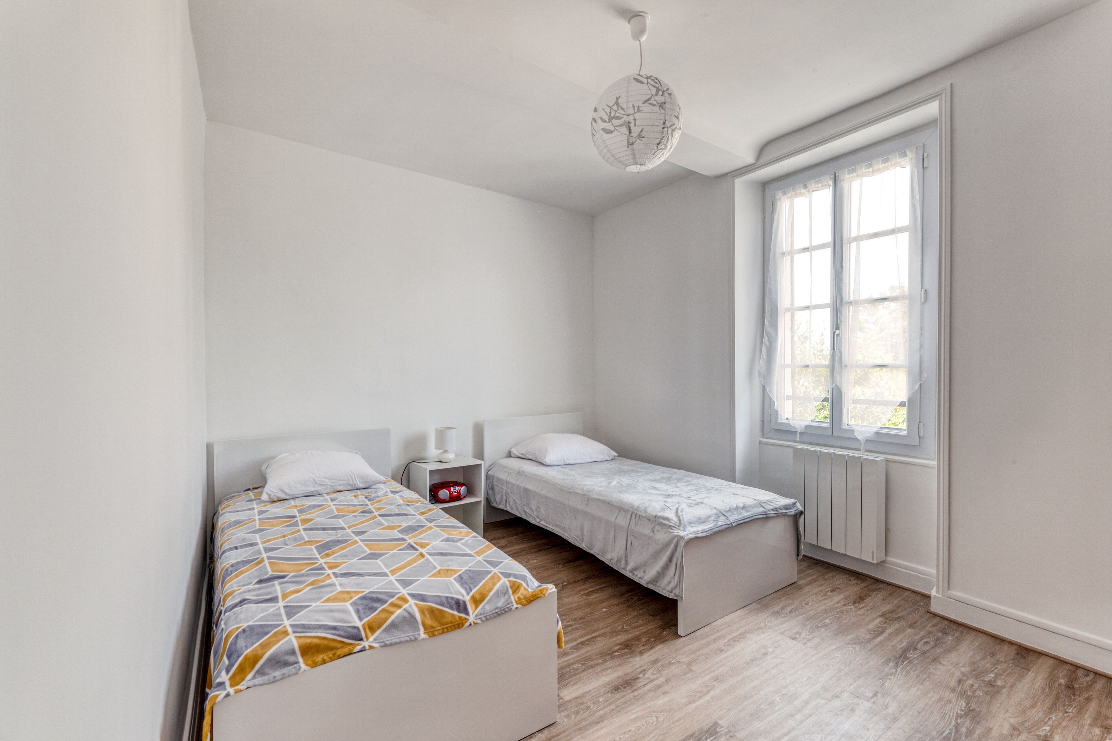 Une chambre avec deux lits, une fenêtre et un radiateur.