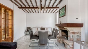 Un comedor con una mesa de madera, sillas grises, una araña y una chimenea de piedra.