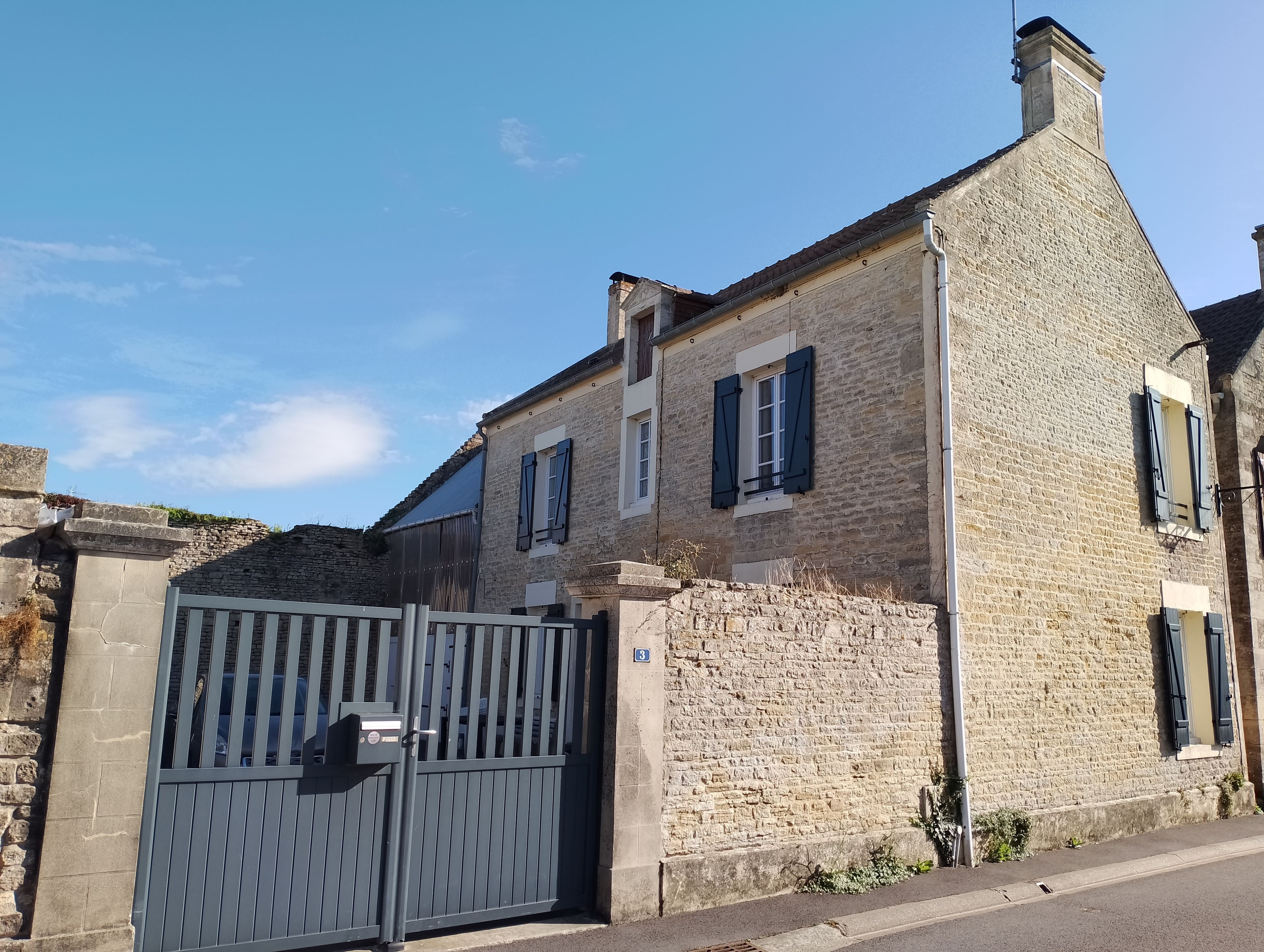 A stone building with a gated entrance, a chimney, and a number '3' on the wall.