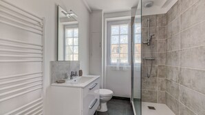 Un baño moderno con cabina de ducha de vidrio, un lavabo blanco y un inodoro.