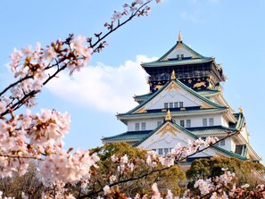 Un castillo japonés tradicional con varios niveles y decoraciones doradas, rodeado de cerezos en flor.